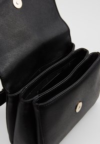 Borsa strutturata nera realizzata in materiale sintetico testurizzato, dotata di chiusura con bottone magnetico e tre scomparti interni.