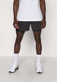 Shorts de sport noirs avec doublure intérieure, portés avec un tee-shirt blanc, des chaussettes blanches et des chaussures de sport blanches avec des accents rouges et noirs.