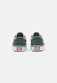 Chaussures Vans en daim vert avec semelle blanche et bande latérale noire emblématique. Logo Vans rouge sur le talon. Design simple avec une forme plate.