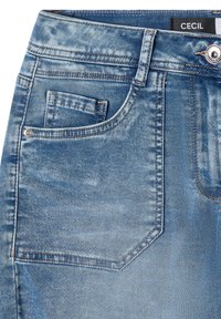 Jean en denim bleu en gros plan montrant la poche avant avec petite poche à monnaie, passants de ceinture, bouton métallique et une étiquette noire avec texte blanc "CECIL".