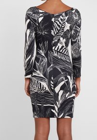 Svartvit klänning med långa ärmar, V-ringning och ett blad- och blommönster. Slät tyg med kontrasterande mönster på varje sida.