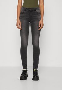 Sorte skinny jeans med en falmet vask, femlomme-design og knaplukning. Bæret med sorte chunky sneakers og en olivengrøn top.