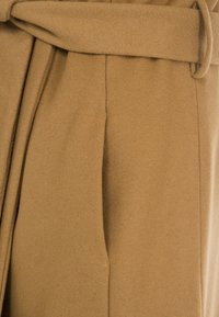 Tejido de mezcla de lana marrón con cinturón de lazo. Presenta una textura suave con pliegues y una forma estructurada, adecuada para prendas de abrigo.