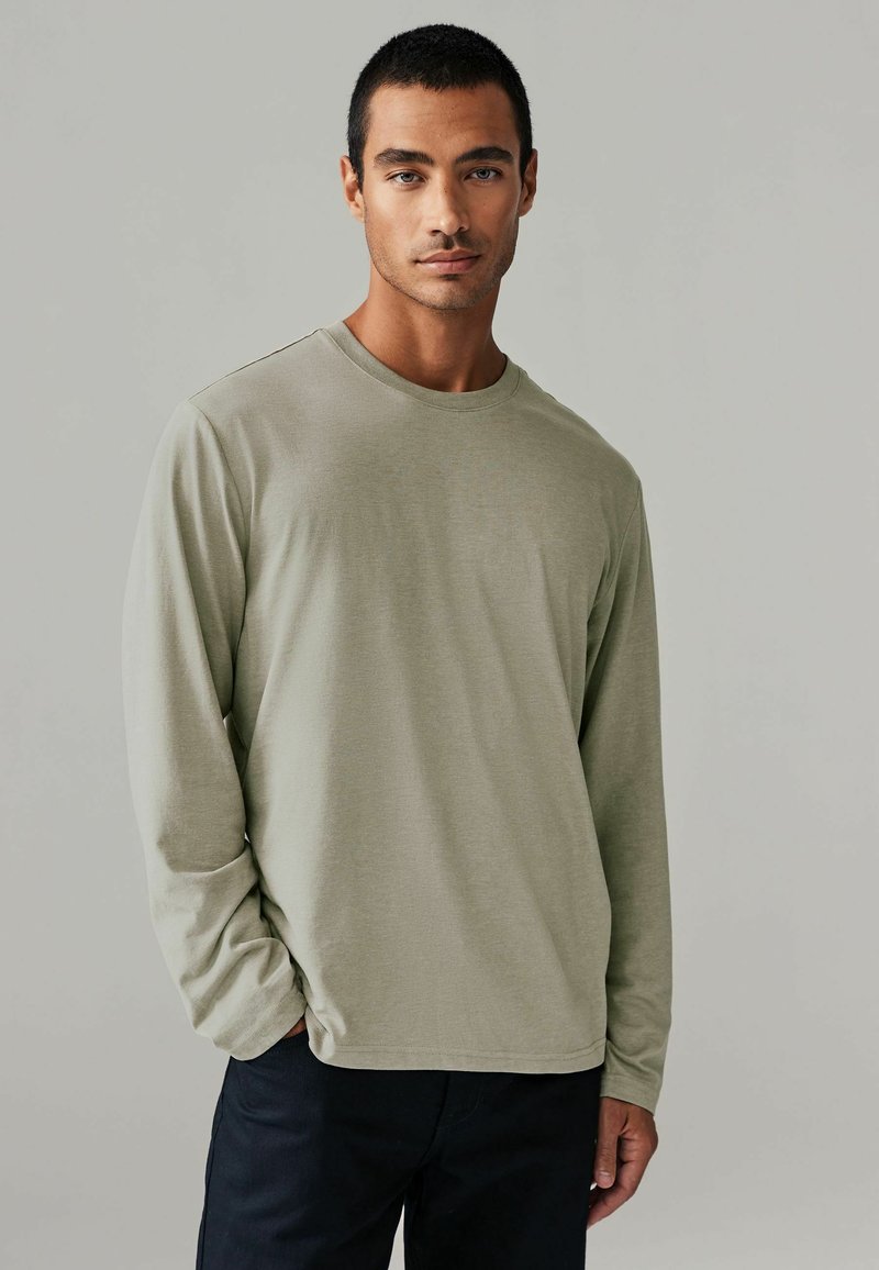 Langsleeve shirt met ronde hals in een licht olijfgroene stof. Zachte textuur met een relaxte pasvorm, voorzien van minimale stikseldetails en zonder patronen.