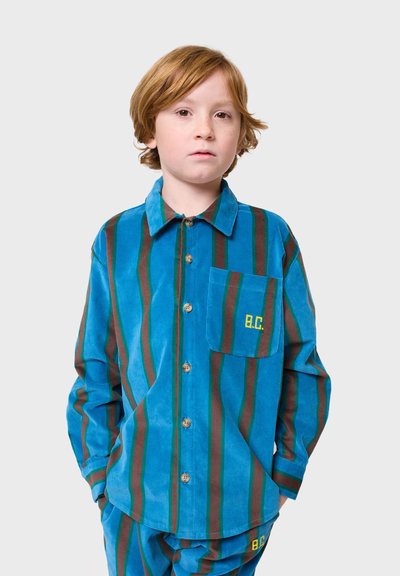 Plava kord košulja s smešnim i zelenim prugama. Ima ovratnik, kopčanje na dugmad i džep sa izvezenim "B.C.".