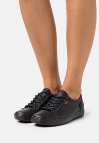 Schwarze Ledersneaker mit runder Spitze, Schnürung, niedrigem Profil und strukturiertem Gummisohle. Seitliches Logodetail, glatte Oberfläche.