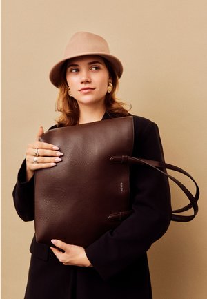Brown leather tote bag with textured surface, two shoulder straps, and a simple design. The bag is held against a neutral background.
