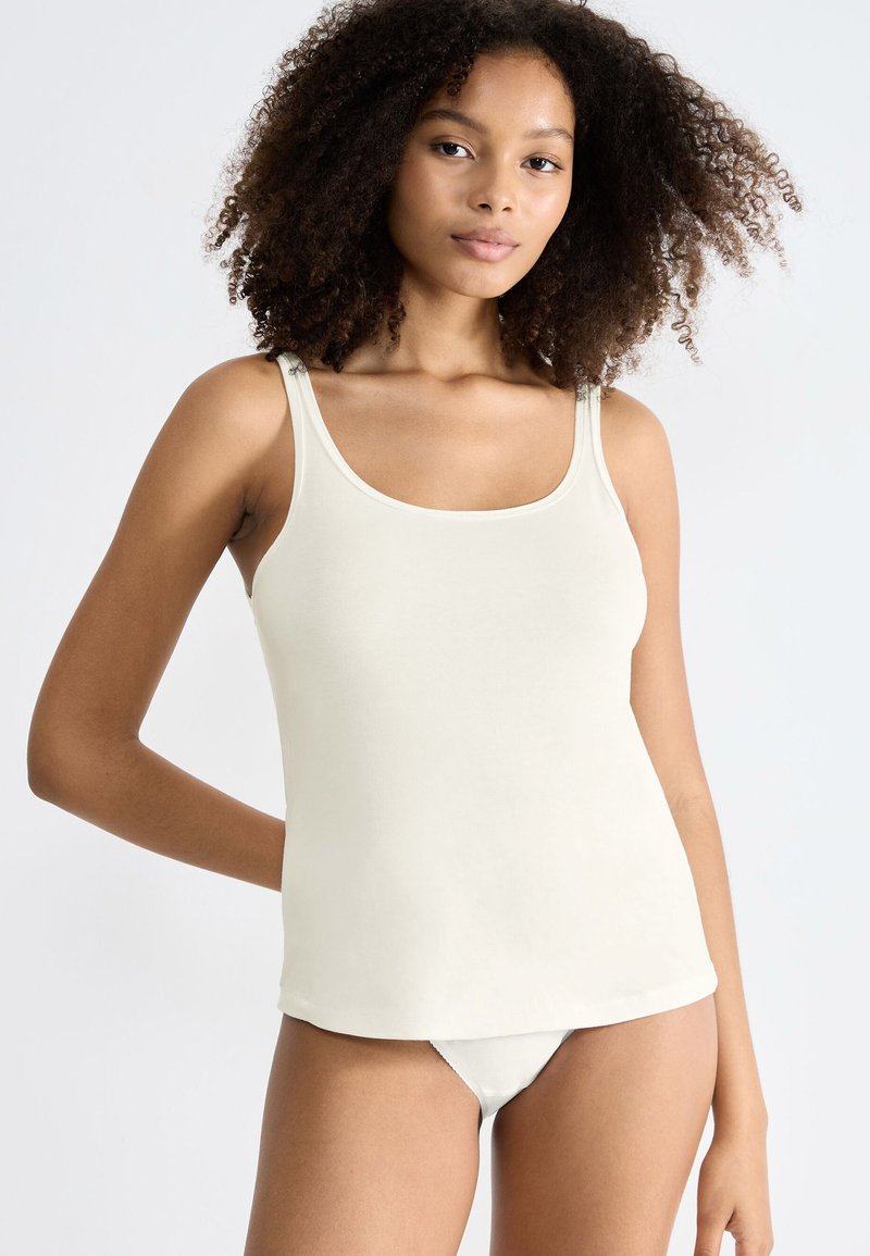 Top a manica corta color crema con scollo rotondo, forma aderente e spalline sottili, realizzato in tessuto liscio, abbinato a lingerie coordinata.