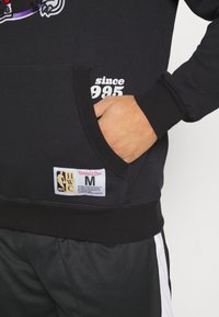Czarny hoodie z kieszenią z przodu, z białym napisem "since 1995" oraz metką z logiem NBA. Żebrowane mankiety i dół.