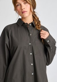 Camicia button-up a maniche lunghe in cotone grigio scuro, con colletto a punta, tasca frontale e orlo arrotondato. I bottoni bianchi aggiungono un contrasto.