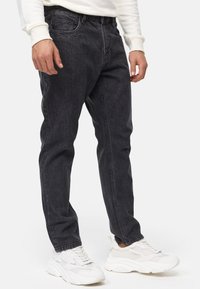 Jeans de mezclilla oscura con un corte relajado, diseño de cinco bolsillos y un sutil desvanecido, combinados con zapatillas deportivas blancas.
