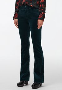 Uitlopende corduroy broek in donkergroen, met een zachte textuur, voorzakken en een getailleerde taille met een knoopsluiting.