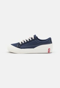 Marina canvas sneakers med vit gummisula, rund tå och snörning framtill. Har kontrasterande vit sömnad och en röd logotypetikett på sidan.