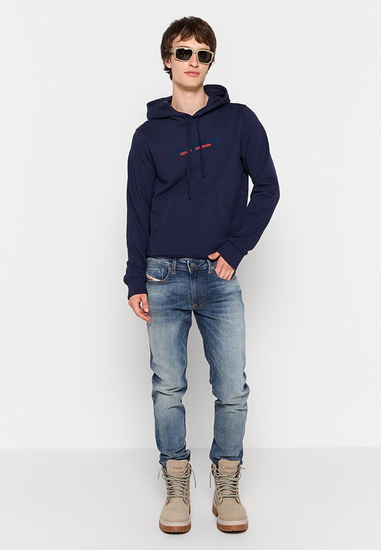 Felpa blu navy con tasca a marsupio e cappuccio con lacci. Indossata con jeans azzurri e stivali color sabbia. Accessoriata con occhiali da sole scuri.