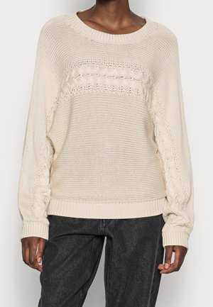 Strikket cremet sweater med en rund halsudskæring, tekstureret mønster over brystet og ribbede manchetter. Har løse, let oversized ærmer.