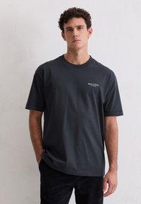 Ciemnoszary t-shirt wykonany z bawełny, z okrągłym dekoltem i krótkimi rękawami. Na przodzie znajduje się małe białe logo.