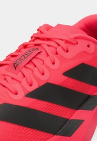 Nærbillede af en klar pink Adidas Adizero løbesko med sorte striber og snørebånd, der viser brandnavnet på tungen.