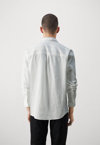 Lichtgrijs langarmshirt met een textuurpatroon, knopenmanchetten en een ronde zoom. Bevat verticale strepen langs de achterkant.