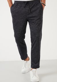 Dark gray jogger pants made of textured fabric, featuring an elastic waistband with drawstring and side pockets, paired with white sneakers.