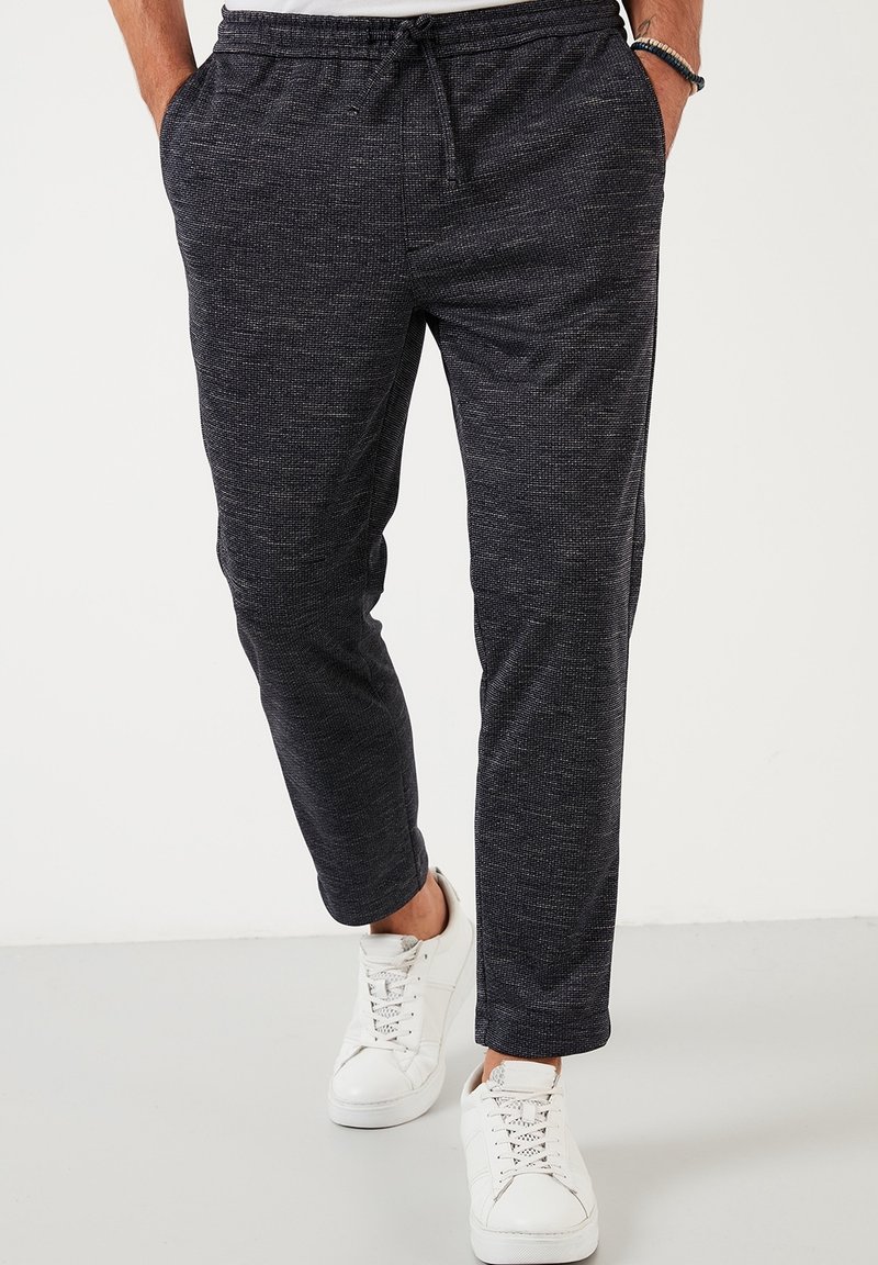 Dark gray jogger pants made of textured fabric, featuring an elastic waistband with drawstring and side pockets, paired with white sneakers.