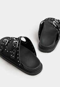 Czarne sandały z nitowanymi paskami, z projektowaniem na wsuwkę i teksturowaną podeszwą. Klamry podkreślają detale pasków.