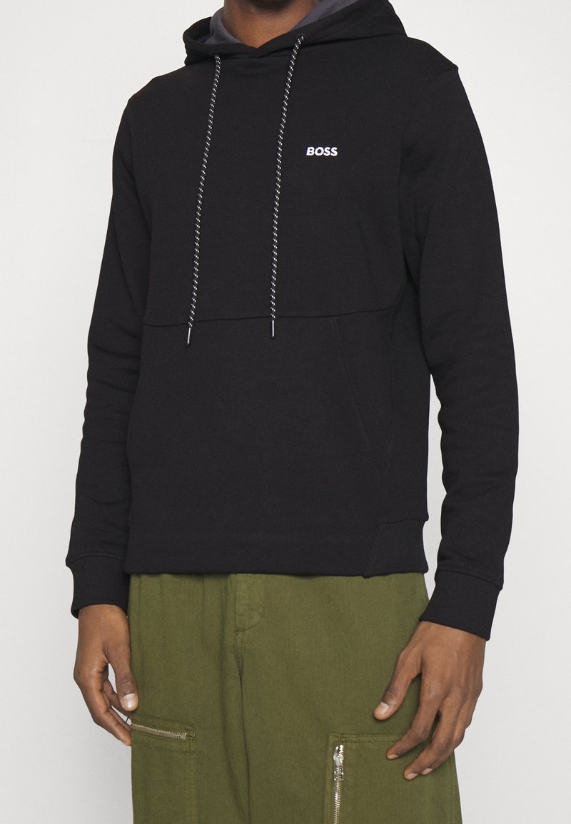 Sweat à capuche en coton noir avec une poche frontale, des cordons ajustables et un petit logo blanc "BOSS". Associé à un pantalon cargo vert olive avec des fermetures éclair.