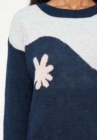 Marineblauer Pullover mit einem weiß-hellrosa floralen Design, ausgestattet mit einem strukturierten Strick und einem runden Kragen.