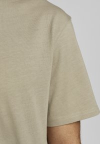 Beige short-sleeve t-shirt with a smooth texture, featuring a crew neckline and subtle stitching detail along the sleeves.