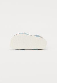 Ljusblå sandaler med justerbara remmar, strukturerad sula och platt design. Har en slät, vit sula med ett mönstrat grepp.