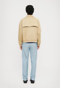 Bežna jakna z velikim zadnjim nastavkom, rebrastimi manšetami in robom. Svetlo modre prugaste hlače in črne čevlje dopolnjujejo videz.