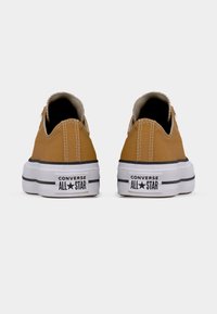 Καφέ παπούτσια slip-on από καμβά με λευκή λαστιχένια σόλα. Διαθέτουν μαύρη ρίγα και το λογότυπο "Converse All Star" στη φτέρνα.