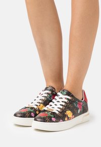 Baskets à imprimé floral multicolore sur fond noir, lacets blancs, accents rouges et semelle en caoutchouc texturée. Détail du logo sur le côté.