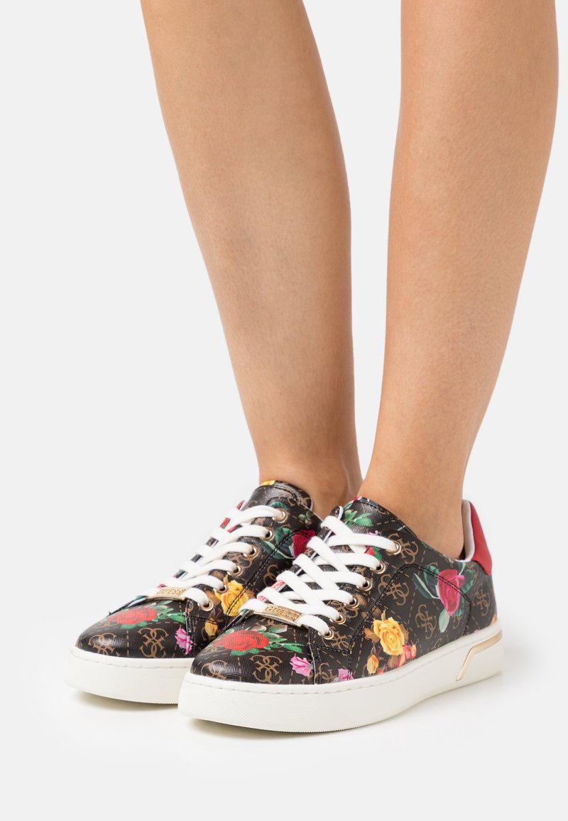 Baskets à imprimé floral multicolore sur fond noir, lacets blancs, accents rouges et semelle en caoutchouc texturée. Détail du logo sur le côté.