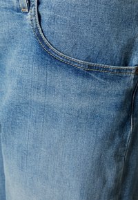 Tecido de denim azul claro com uma textura suave. Apresenta uma abertura de bolso curva e costura amarela contrastante ao longo da costura.
