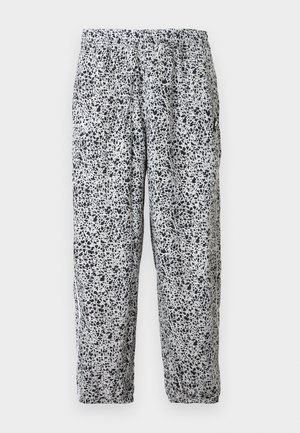 Valkoiset joustovyötäröiset housut mustilla epäsäännöllisillä pilkkukuoseilla ja joustavilla lahkeensuut roikkumassa yksiväristä taustaa vasten.