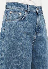 Lichtblauwe spijkershort met een vervaagd, patroonontwerp. Voorzien van vijf zakken en metalen accenten met zichtbare stiknaden.