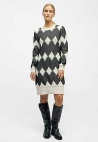 Robe en tricot à manches longues noir et blanc avec un motif en losange, des poignets côtelés et un ourlet qui tombe au-dessus du genou.