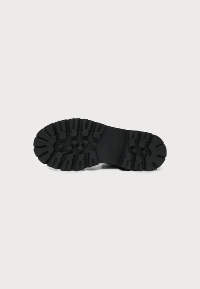 Semelle de botte noire avec un motif de crampons profond et robuste conçu pour une forte adhérence sur différentes surfaces.