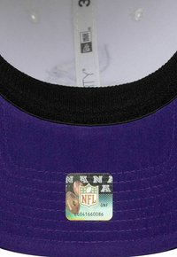 Gorra púrpura con visera negra, con detalles de costura y una etiqueta de la NFL que muestra un logo e imágenes de fútbol. Interior forrado en blanco.