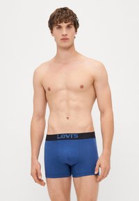 Modré bavlnené boxerky s čiernym pásom, na ktorom je modré logo Levi's. Hladký povrch, priliehavý strih a dĺžka do polovice stehna.