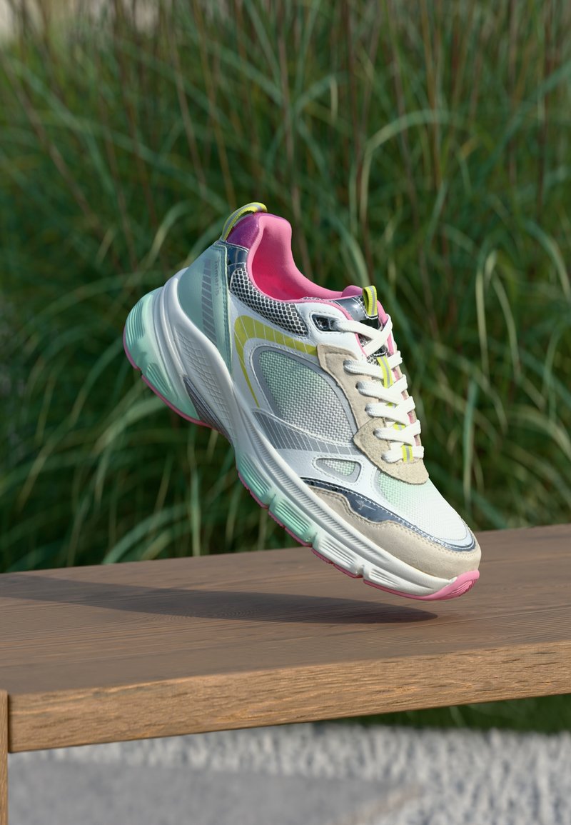 Baskets blanches et pastel avec un intérieur rose et des accents jaunes flottant au-dessus d'un banc en bois, des plantes vertes en arrière-plan.