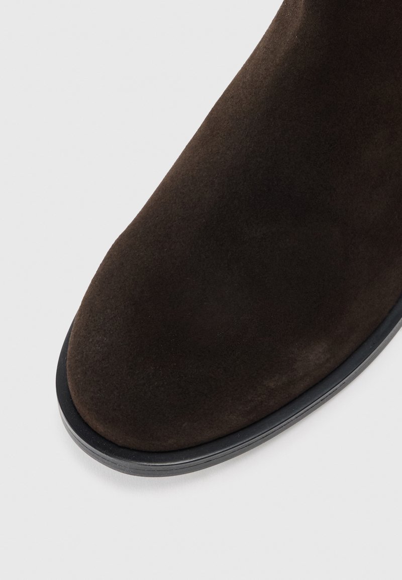 Braune Wildleder-Ankle-Boots mit runder Spitze und schwarzer Gummisohle, die über eine glatte, weiche Textur und klare Linien verfügen.