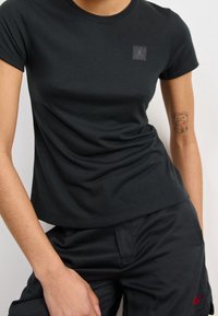 Černé přiléhavé tričko s krátkými rukávy, kulatým výstřihem a malou nášivkou s logem Jordan na hrudi. Hladká látka, v kombinaci s černými kalhotami.