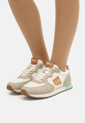 Zapatillas beige y blancas con un acento azul claro. Presentan materiales de ante y malla, punta redonda, suela plana y logo en el lateral.