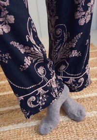 Jūriniai keliaraiščiai su rožiniu gėlių raštu ir apvadu; pilkos kojinės ant tekstūrinio austos kiliminės dangos. Dėmesys audinių raštams ir spalvų kontrastui.