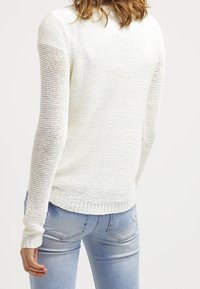 Witte gebreide trui met een textuurpatroon en lange mouwen, aangevuld met een geribbelde zoom en een fitted stijl. Achteraanzicht.