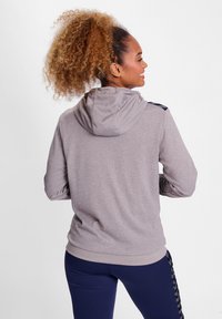 Grijze hoodie van textuur stof, met een capuchon en zwarte accenten op de schouders, gecombineerd met marineblauwe leggings.