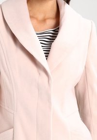 Ljust rosa blazer med texturerad yta, stor krage och framfickor. Bärs över en svartvit randig topp.