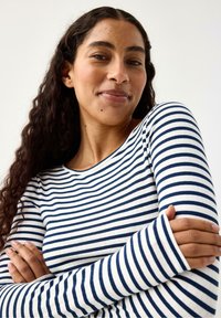 Långärmad topp med marinblå och vita horisontella ränder, ribbad textur och rund halsringning. Tyget verkar mjukt och lätt.