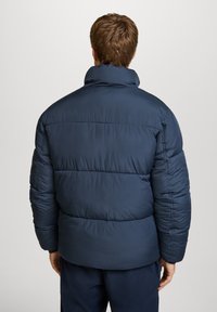 Giacca puffer blu navy con collo alto, design trapuntato e texture morbida, caratterizzata da una vestibilità comoda e una finitura liscia.